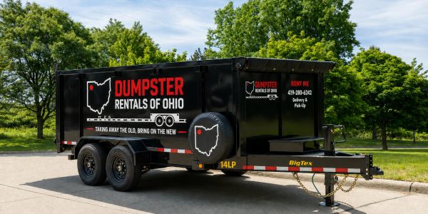 Black dumpster rental trailer parked outdoors near trees.