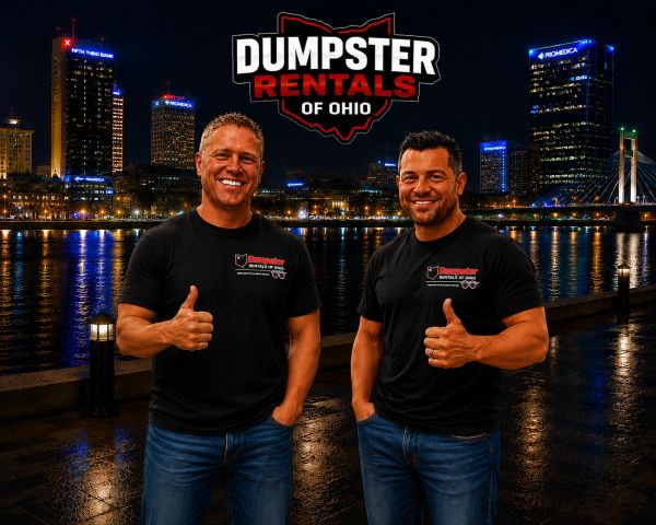 Two men smiling and giving thumbs up by the river at night.