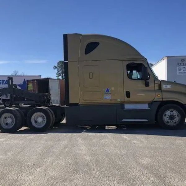 Golden brown semi-truck parked on asphalt under a clear blue sky.
