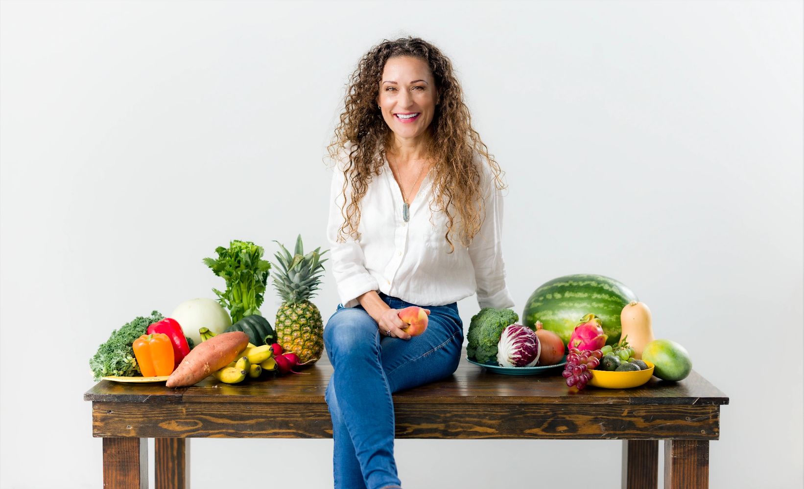 A woman is sitting at a table, holding fruits in her hands, and the table is also with fruits.