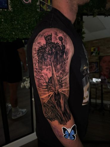 Detailed black and gray tattoo of a dark, armored king wielding a mace on upper arm.