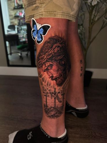 Realistic tattoo of Jesus with three crosses on the lower leg.