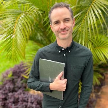 Person standing with a laptop in front of green, leafy background