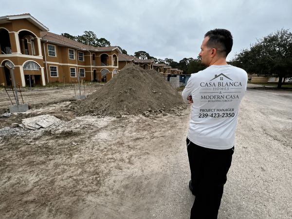 Man in a white shirt standing at a construction site with buildings in the background.
