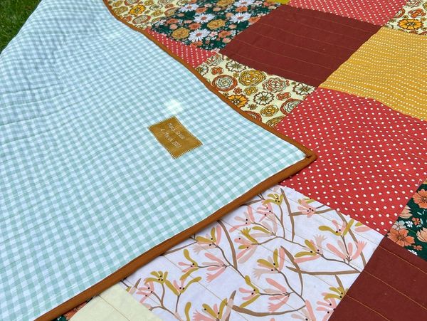 Colorful patchwork quilt spread on grass with a green gingham backing.