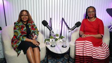 Two women sitting in armchairs with microphones for a podcast or interview.