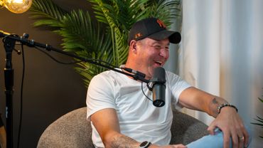 Man laughing during a podcast recording with microphone and casual attire.