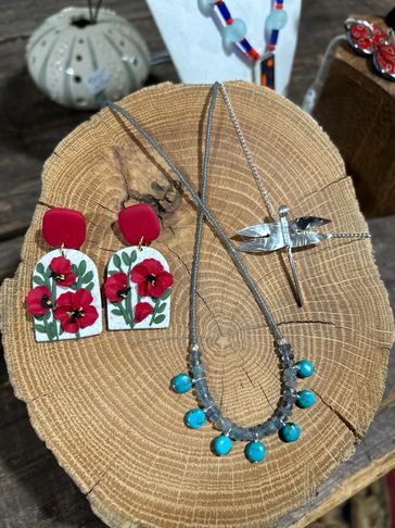 Handcrafted jewelry displayed on a wooden slab, featuring floral earrings and turquoise bead necklace.