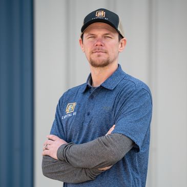 Man wearing a blue Capital K shirt and cap with arms crossed.