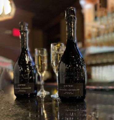 Two bottles of sparkling wine and two filled champagne flutes on a bar counter.