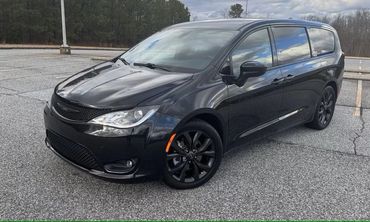 Sleek black minivan parked on a paved area with trees in the background.