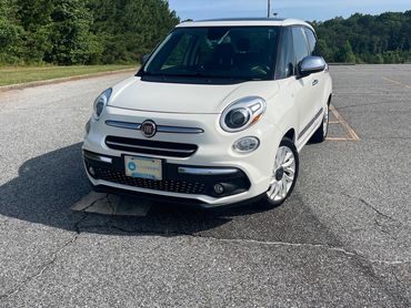 White Fiat 500L parked in an empty parking lot on a sunny day.
