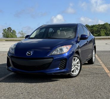 Blue Mazda sedan parked in an outdoor parking lot under a partly cloudy sky.