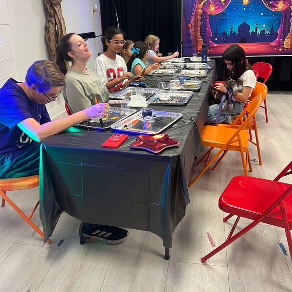Children engaged in a bead crafting activity at a long table.
