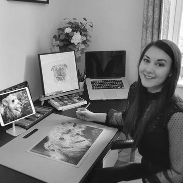 Female artist in studio working on drawing of a grey deerhound. Laptop and Ipad in background