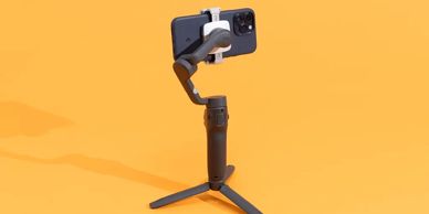 Smartphone mounted on a compact tripod with a gimbal stabilizer against an orange background.
