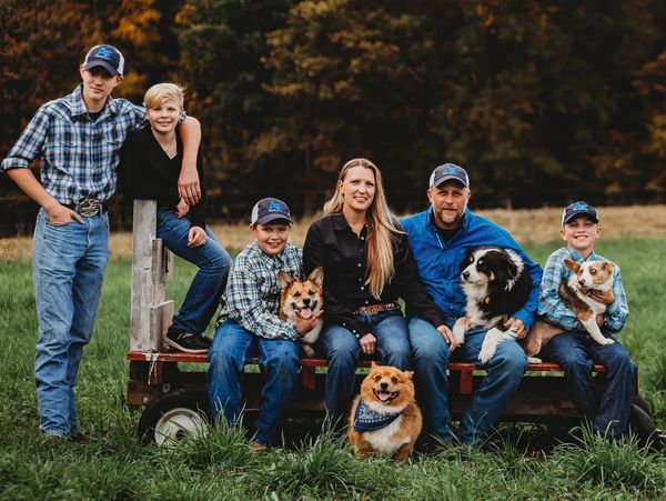Family portrait with three dogs in a grassy field.