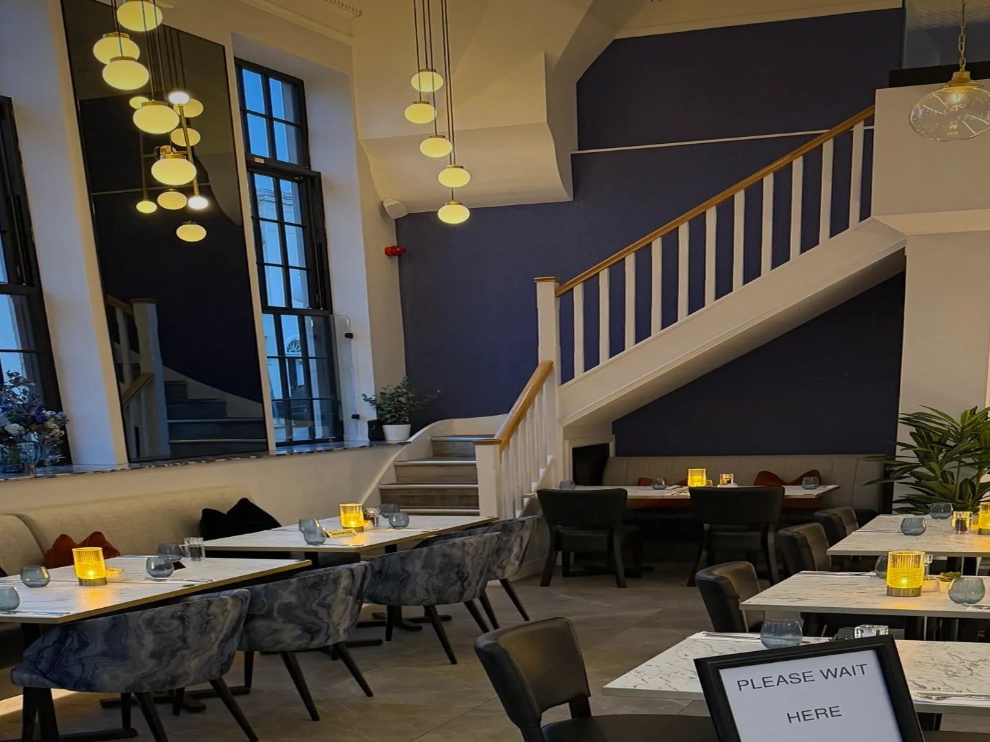 Elegant restaurant interior with cozy lighting and a 'Please Wait Here' sign.