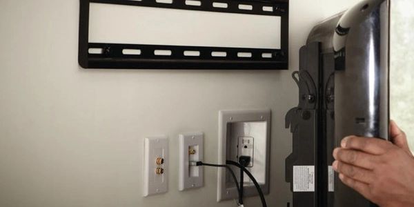 Hand adjusting TV near wall outlets and cables.
