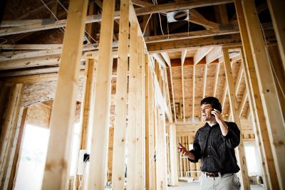 A man talks on the phone inside a wooden house under construction.