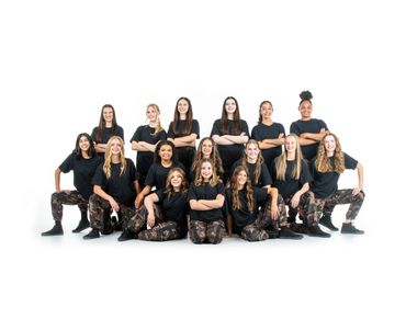 Group of young women in black shirts and camouflage pants posing confidently.