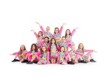 A group of young girls in colorful dance costumes posing joyfully in a pyramid formation.