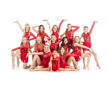 A group of young dancers in red sequined costumes posing cheerfully.
