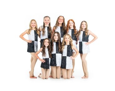 A group of eight girls in black and white sequin dresses posing together.