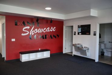 Dance studio lobby with red accent wall, bench, water fountains, and restrooms.