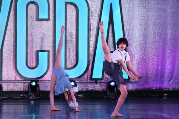 Two young dancers performing impressive leg lifts on stage.