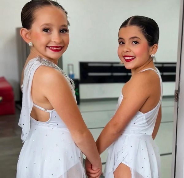 Two young girls in white dance costumes holding hands and smiling.