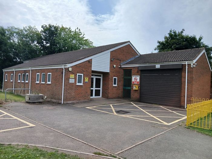 A brick building with multiple windows, a parking area, and yellow fencing.