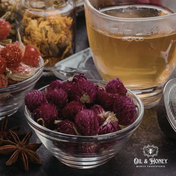 Glass bowl with dried purple flowers beside a cup of herbal tea.