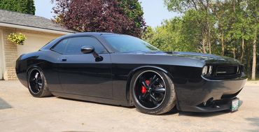 A sleek black Dodge Challenger parked outdoors with tinted windows and custom rims.
