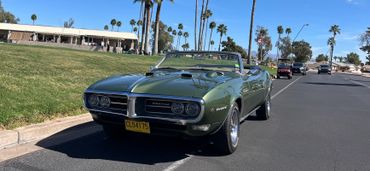 Classic green convertible car parked on a sunny street near a grassy area.