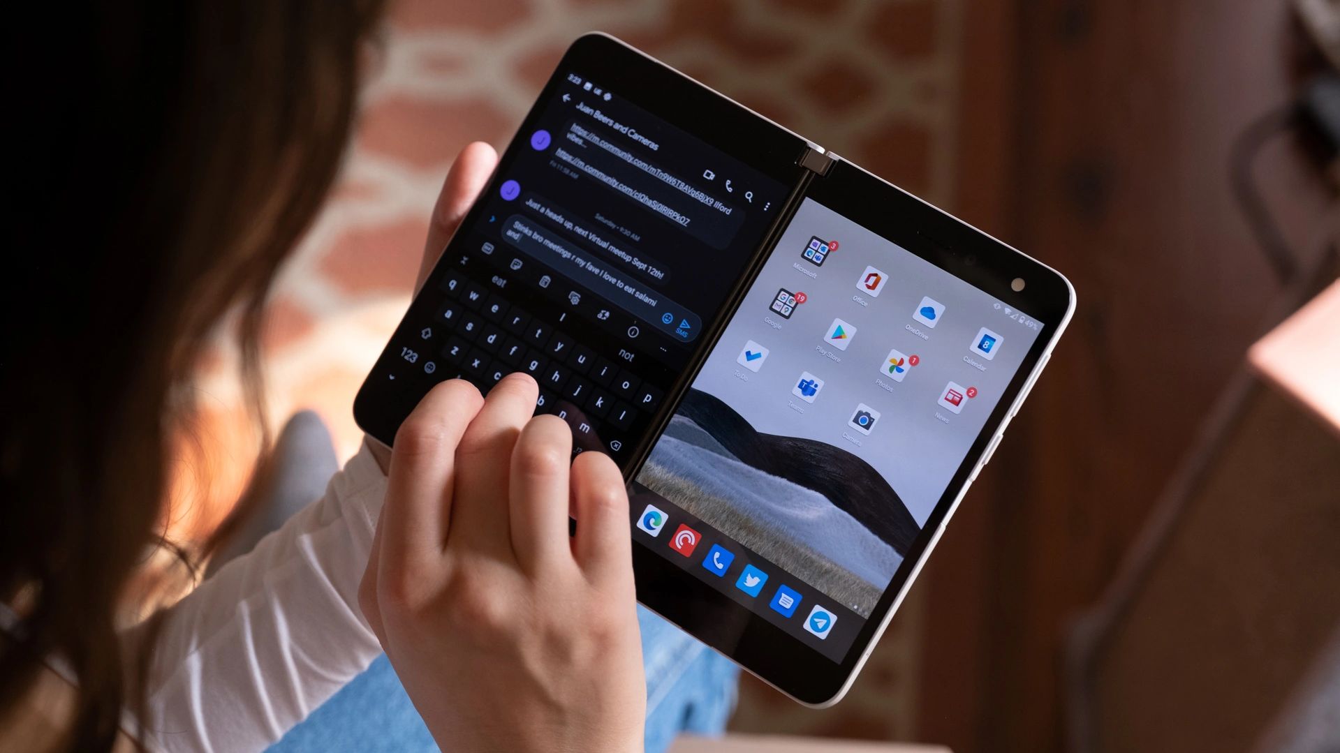 Person typing on a dual-screen foldable device.