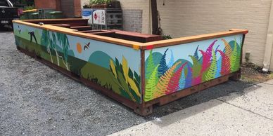 Colorful painted fence with plants and birds around a corner of a building.