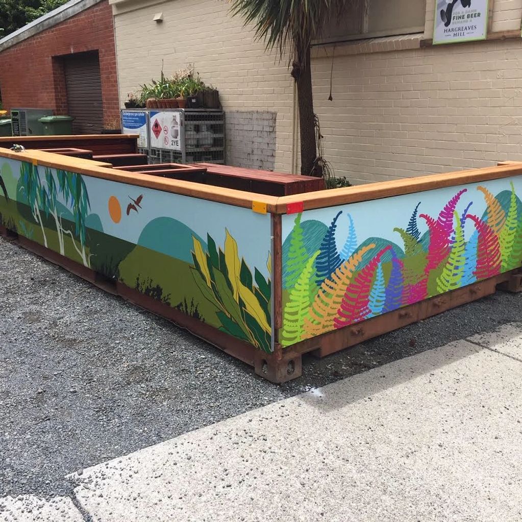 Colorful painted fence with plants and birds around a corner of a building.