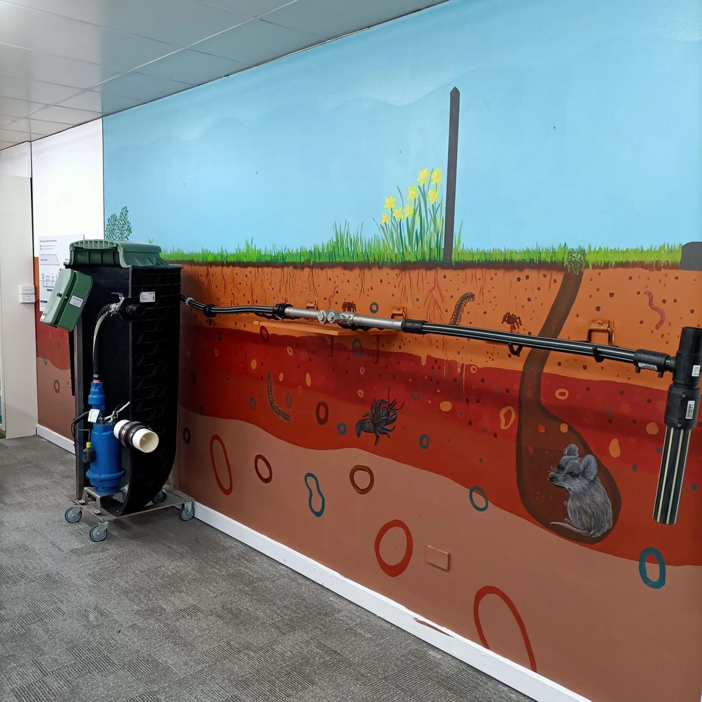 A colorful wall mural depicting soil layers with insects and a mouse, alongside a mechanical device.