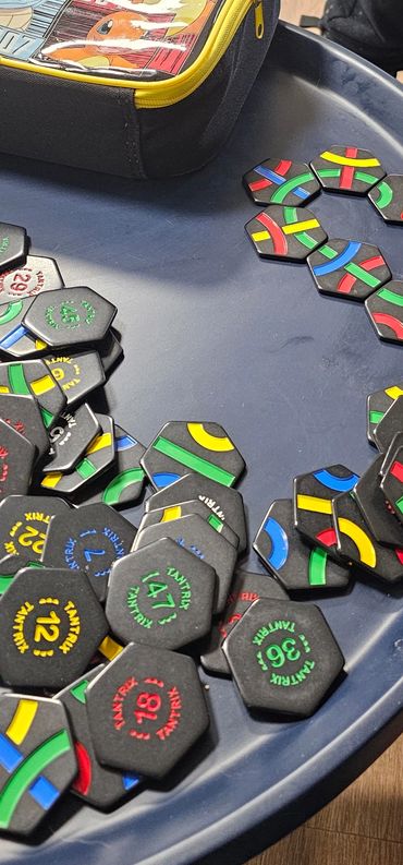 Hexagonal game tokens with colorful stripes on a blue tray.
