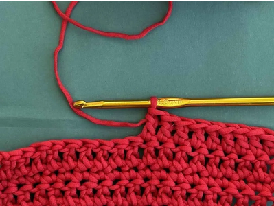 A crochet hook with red yarn in progress.