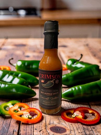 Bottle of Crimson hot pepper sauce with fresh peppers.