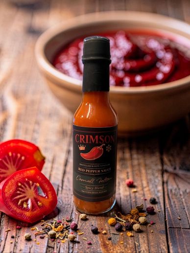 Bottle of Crimson Red Pepper Sauce with fresh peppers and spices.