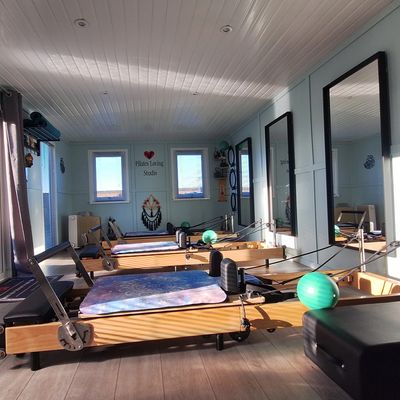 A bright Pilates studio with reformer machines and mirrors along the wall.