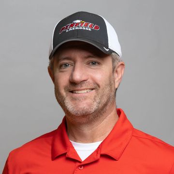 Man in a red lacrosse shirt and gray cap smiling.