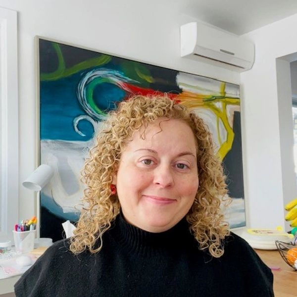 A woman with curly hair smiles in a modern room with colorful artwork.