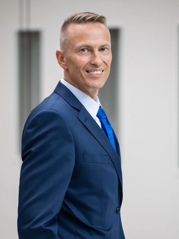 Jarmo Syväri, the author, is standing and wearing a navy blue business suit and tie.