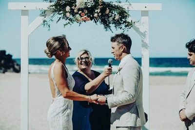 Couple exchanging vows at a beach wedding ceremony under floral arch.