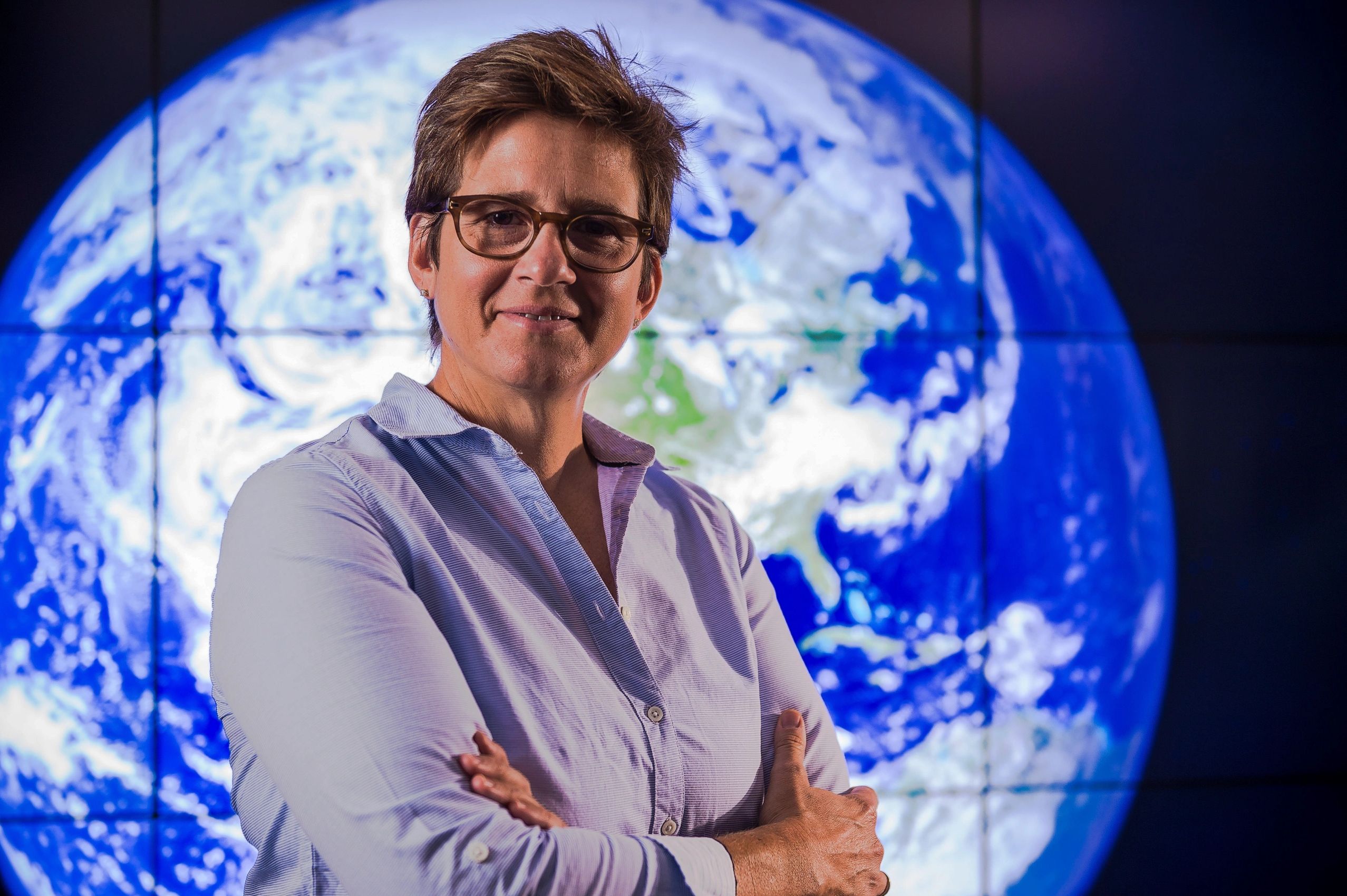 Person standing confidently with arms crossed in front of Earth image.