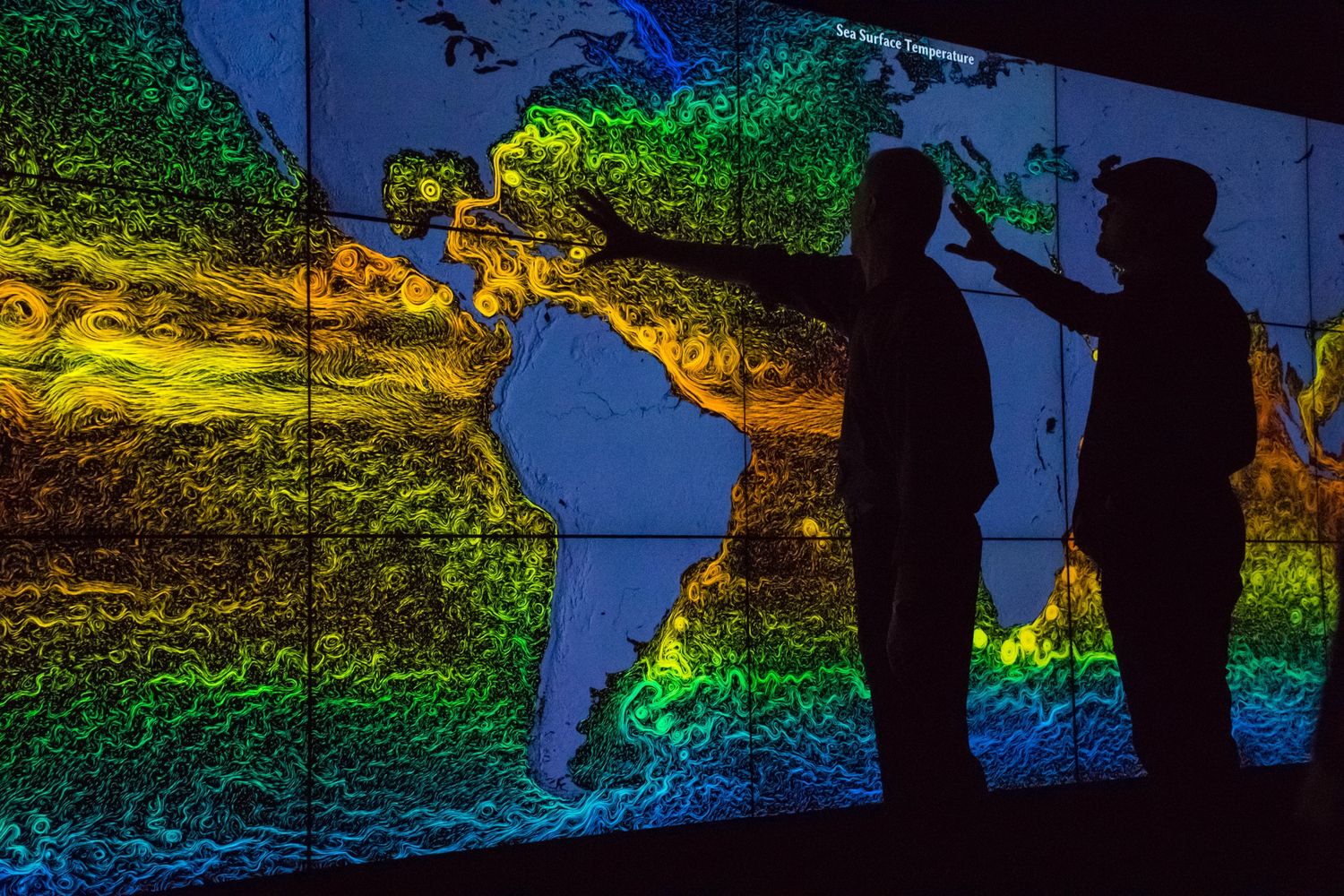 Two people pointing at a colorful sea surface temperature map of the Americas.